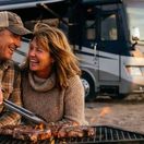Couple cooking in front of their Class A RV