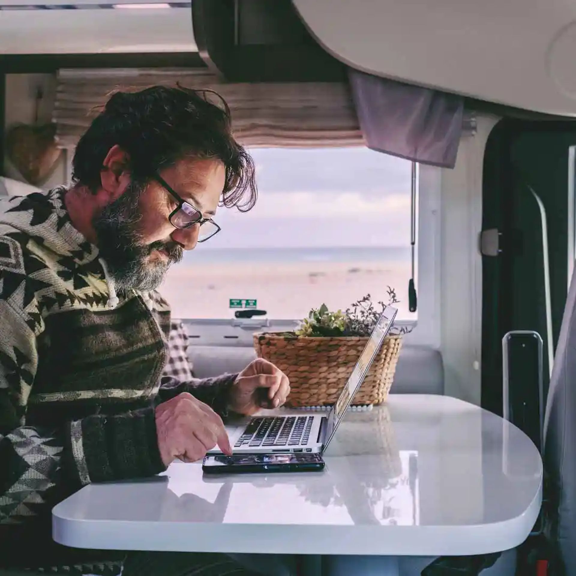 A man using his laptop and phone in his RV.
