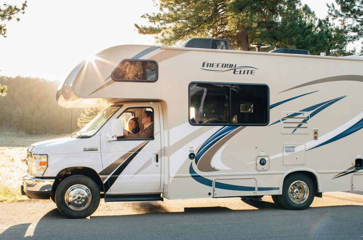 A couple driving in a white Class C RV