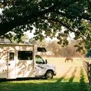 RV parked under the shade in a pasture.