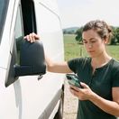 Young woman near her camper RV, checking her phone.